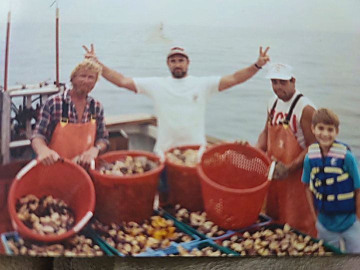 A faded snapshot from the early years: crew on deck behind orange baskets heaped with stone crab claws, a child in a life jacket beside them.