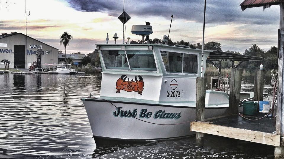 The crab boat Just Be Claws, hull number X-2073, tied to the dock at dusk with a painted stone crab on the bow.