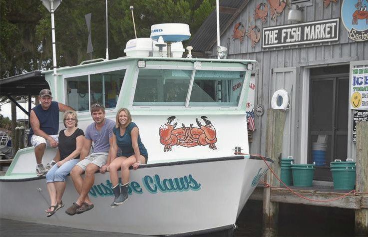 Four members of the Smith family sitting along the bow of Just Be Claws, moored in front of the fish house.